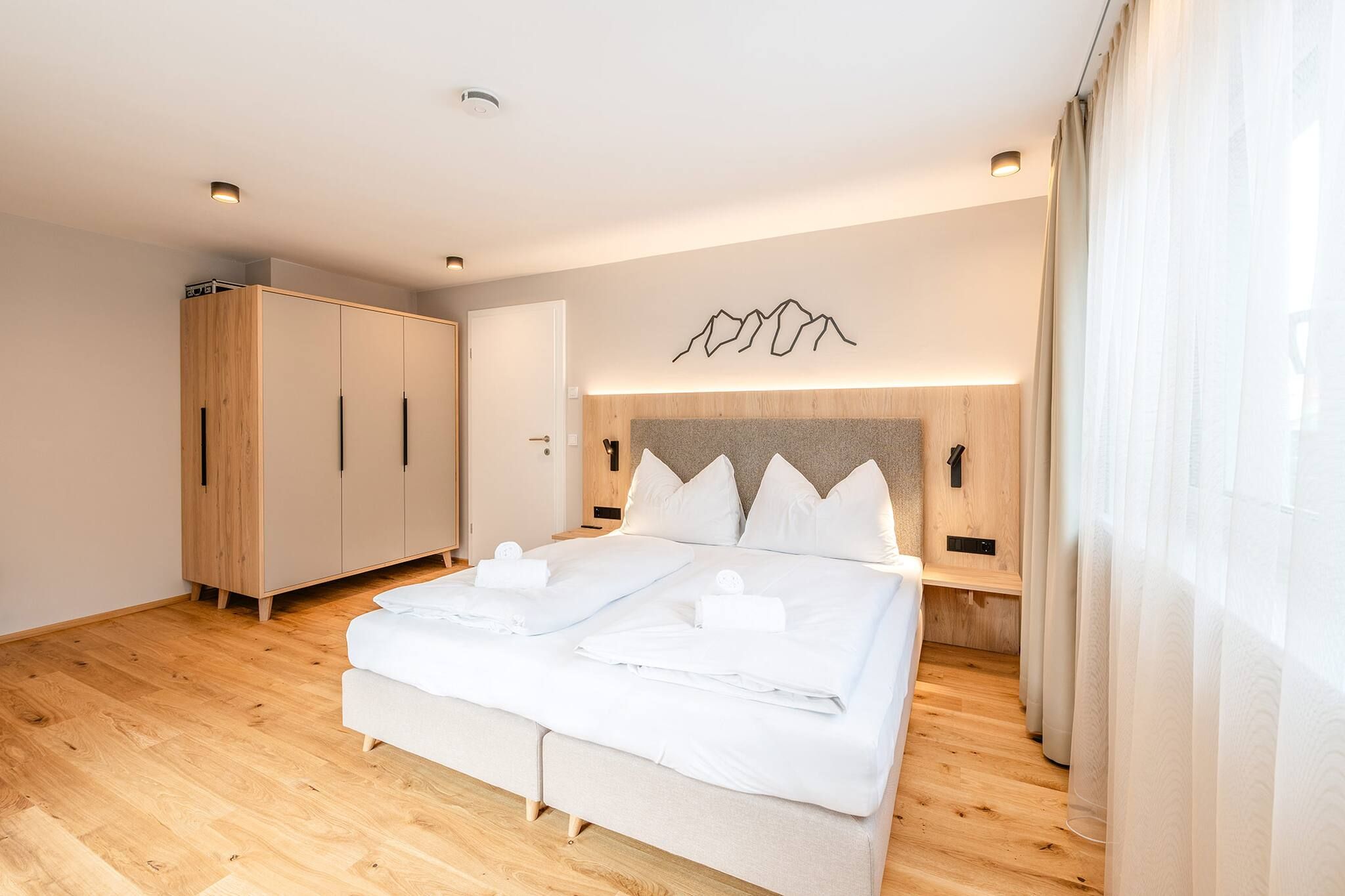 Un dormitorio moderno con una cama grande, un armario de madera y una lámpara fijada a la pared.