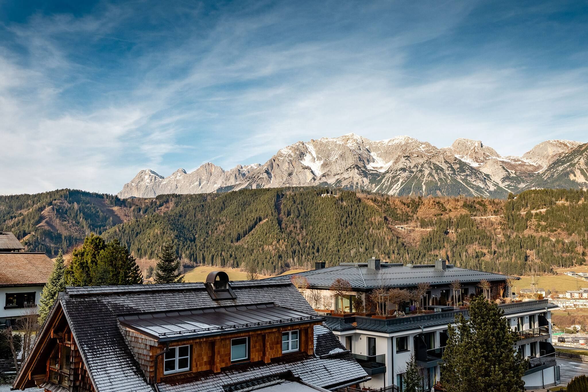 Un pueblo de montaña con casas de madera tradicionales, cielo despejado y picos nevados al fondo.