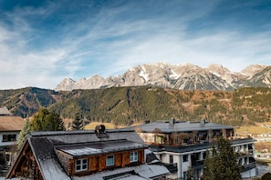 Ein Bergdorf mit traditionellen Holzhäusern, einem klaren Himmel und schneebedeckten Berggipfeln im Hintergrund.