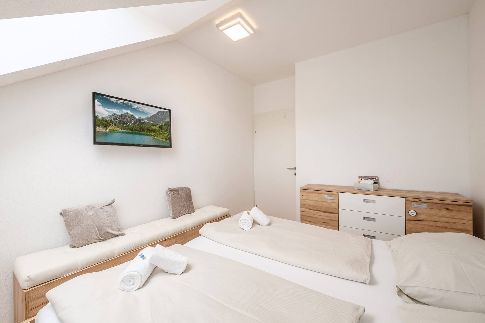 Ein Schlafzimmer mit zwei Betten, einer Holzkommode, einem Flachbildfernseher an der Wand und einem Bild von einer Berglandschaft.