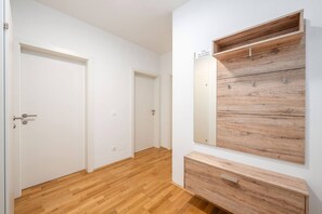 A hallway with wooden flooring, white walls, and a built-in wooden shelf unit with a nameplate.
