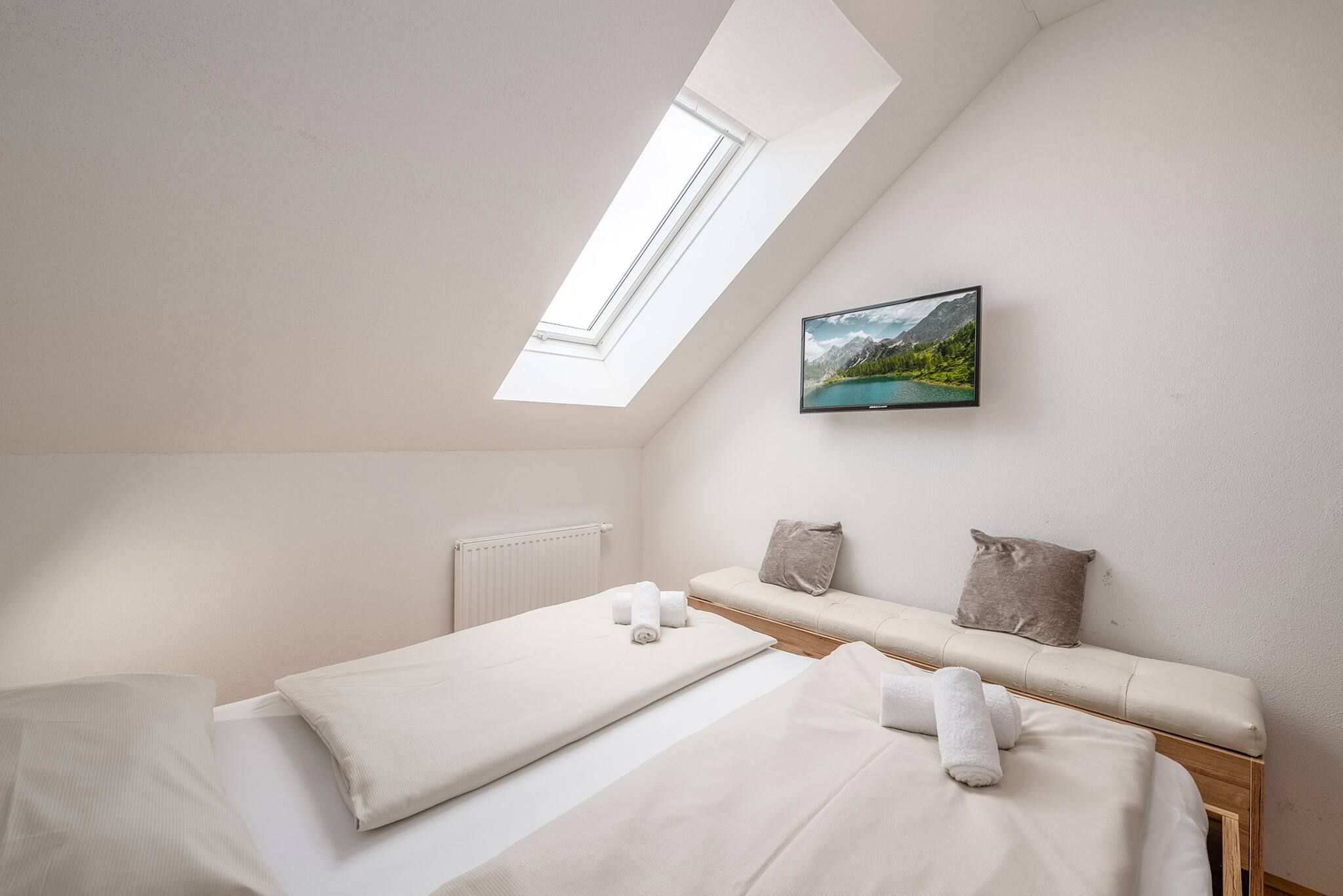Ein Schlafzimmer mit Oberlicht, einem Bett mit weißen Leinen, einem Heizkörper und einem Landschaftsbild.