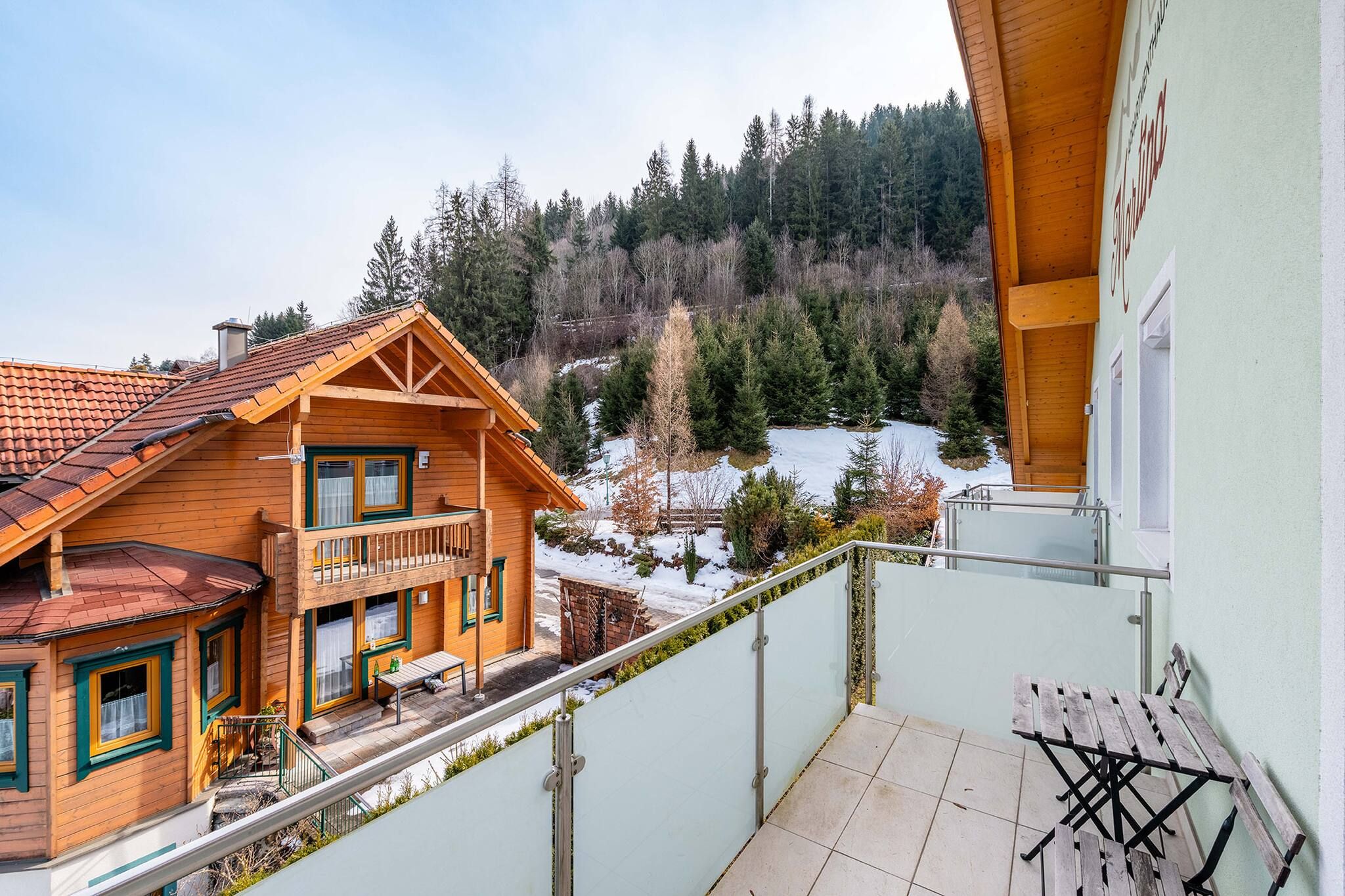 Eine Holzhütte mit einem Balkon mit Blick auf eine verschneite Landschaft und einen Wald.