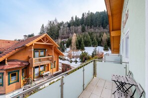 Eine Holzhütte mit einem Balkon mit Blick auf eine verschneite Landschaft und einen Wald.