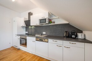 A modern kitchen with white cabinets, a built-in oven, a microwave, a coffee maker, and a toaster.