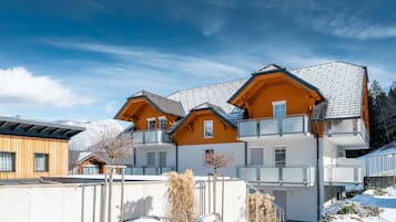 Ein mehrstöckiges Chalet mit geneigtem Dach, Balkonen und verschneiter Landschaft.