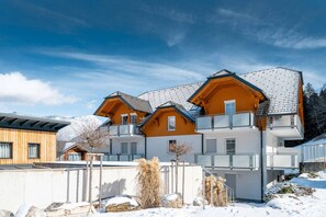 Ein mehrstöckiges Chalet mit geneigtem Dach, Balkonen und verschneiter Landschaft.