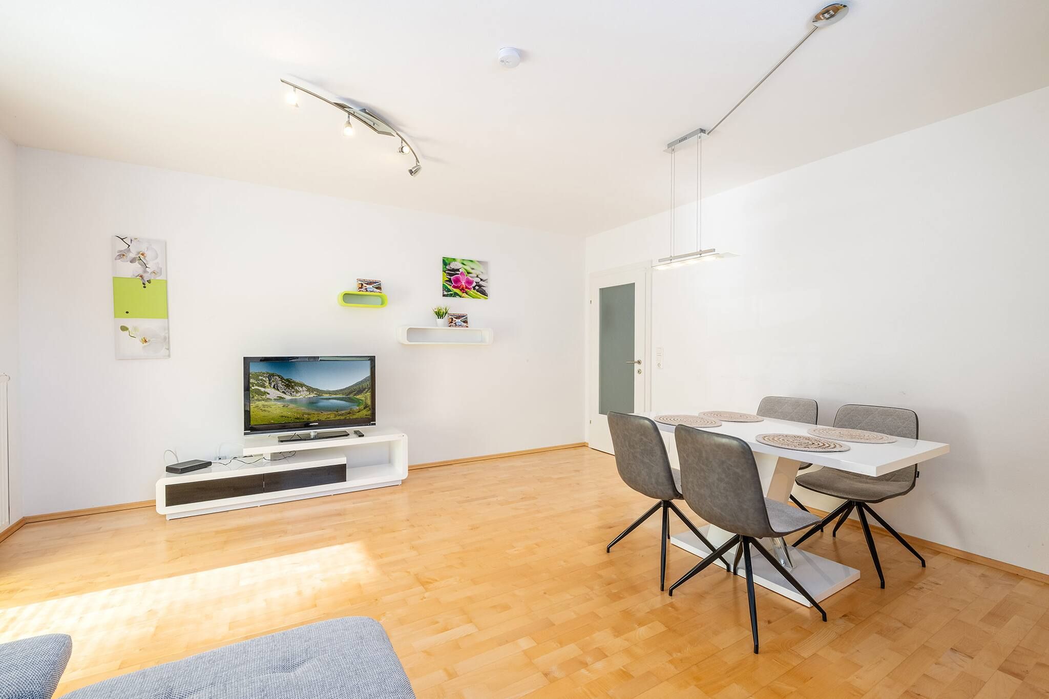 Ein modernes Wohnzimmer mit Flachbildfernseher, einem Esstisch mit Stühlen und einer Couch.