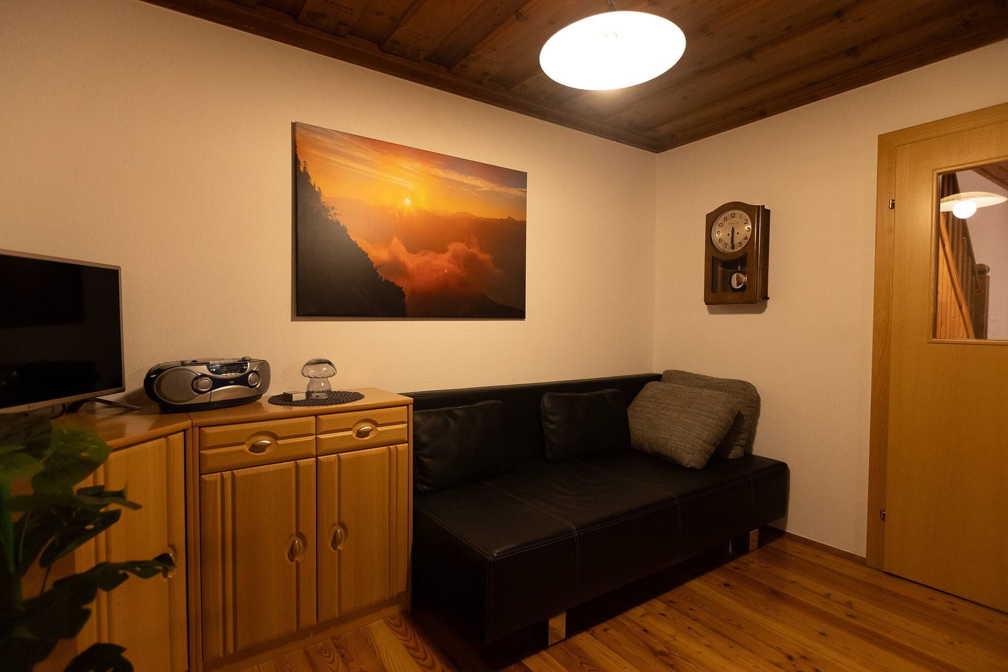 Una stanza accogliente con un armadietto in legno, un divano nero, un quadro del tramonto, una sveglia e una televisione.
