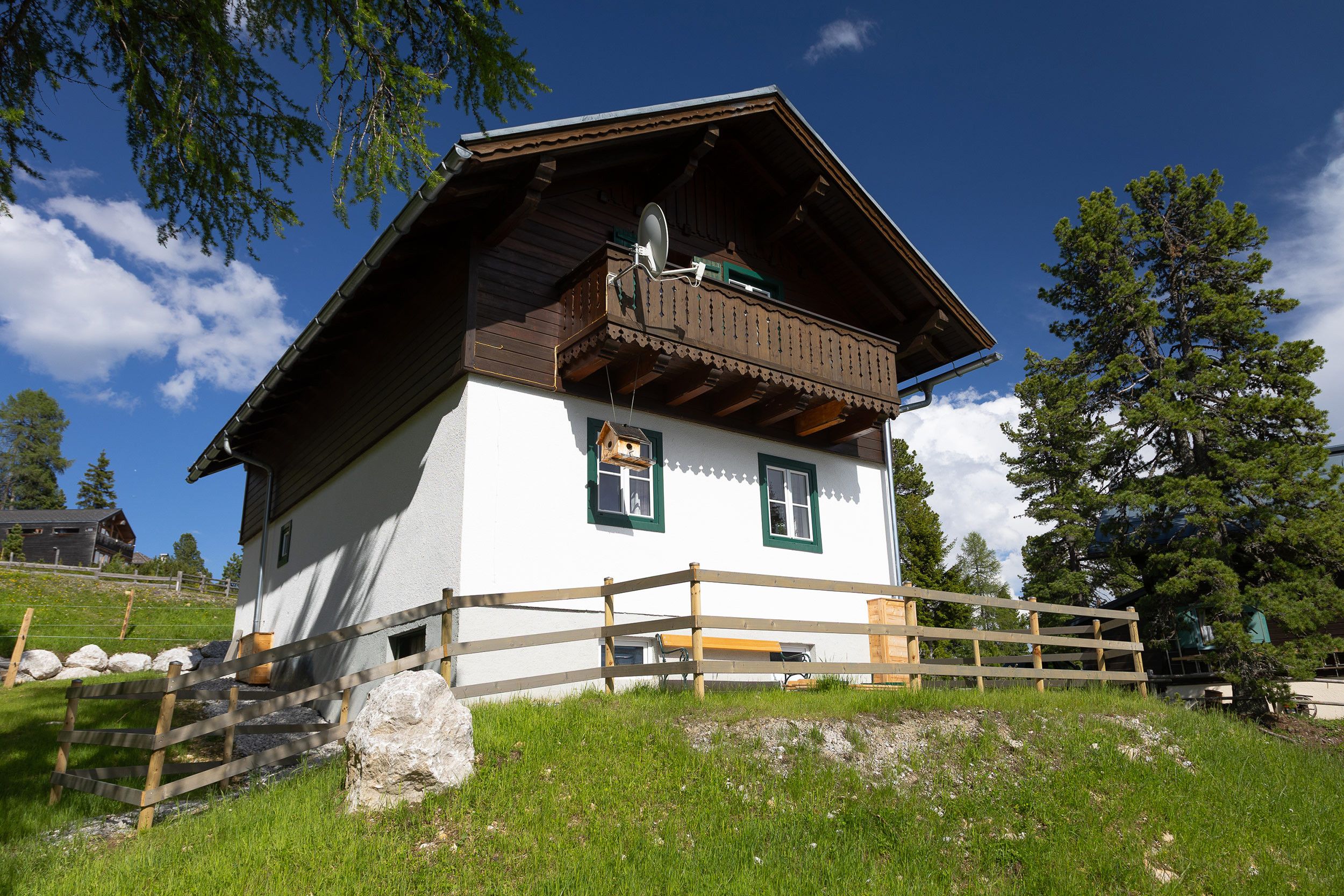 Ein traditionelles Chalet mit Holzbalkon, einer Steinmauer und einem grasbewachsen Vordergrund.