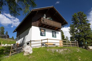 Ein traditionelles Chalet mit Holzbalkon, einer Steinmauer und einem grasbewachsen Vordergrund.