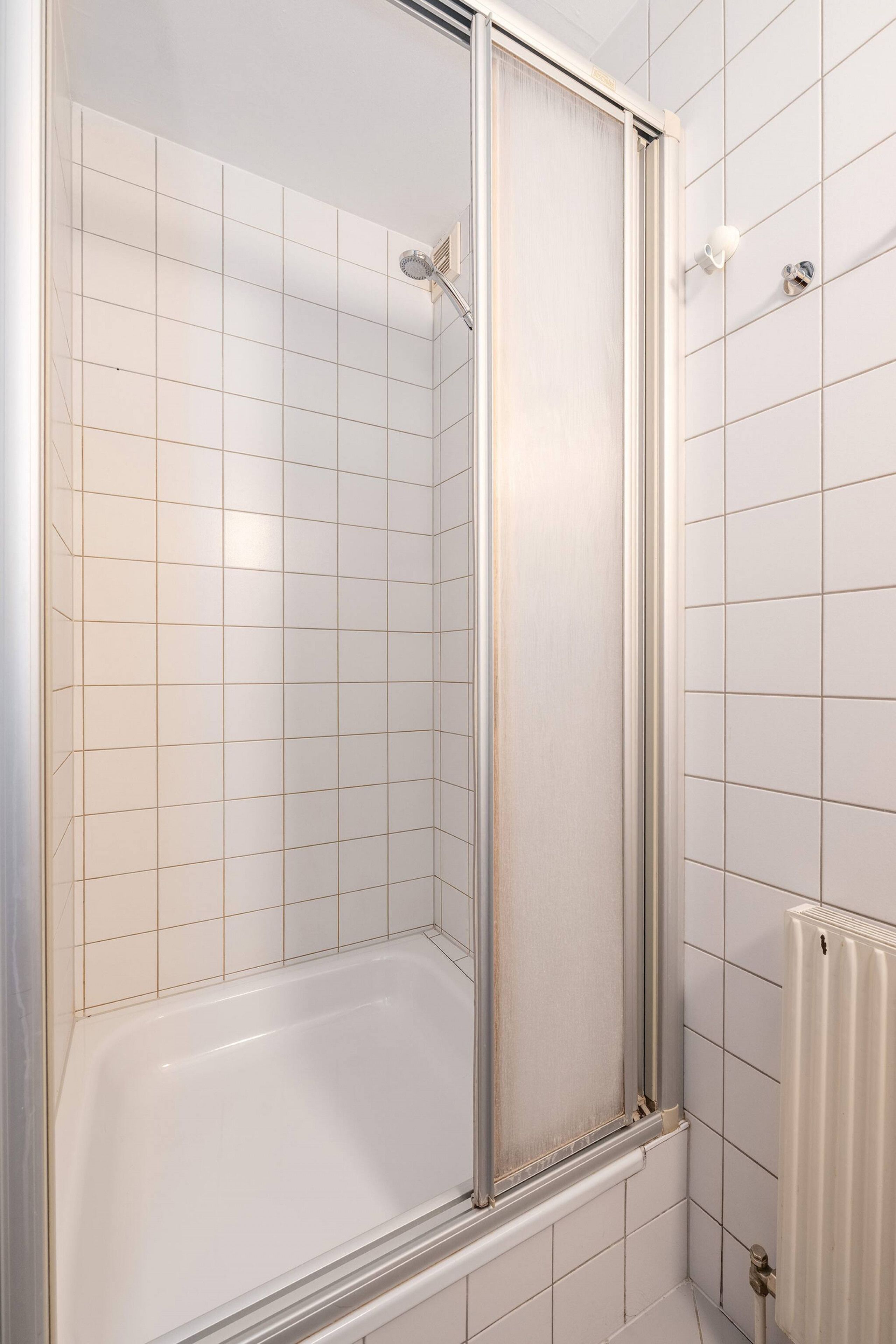 Un baño con paredes de azulejos blancos, cabina de ducha de vidrio y bañera blanca.