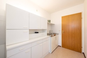 Una cocina pequeña con armarios blancos, un lavamanos y una puerta de madera.