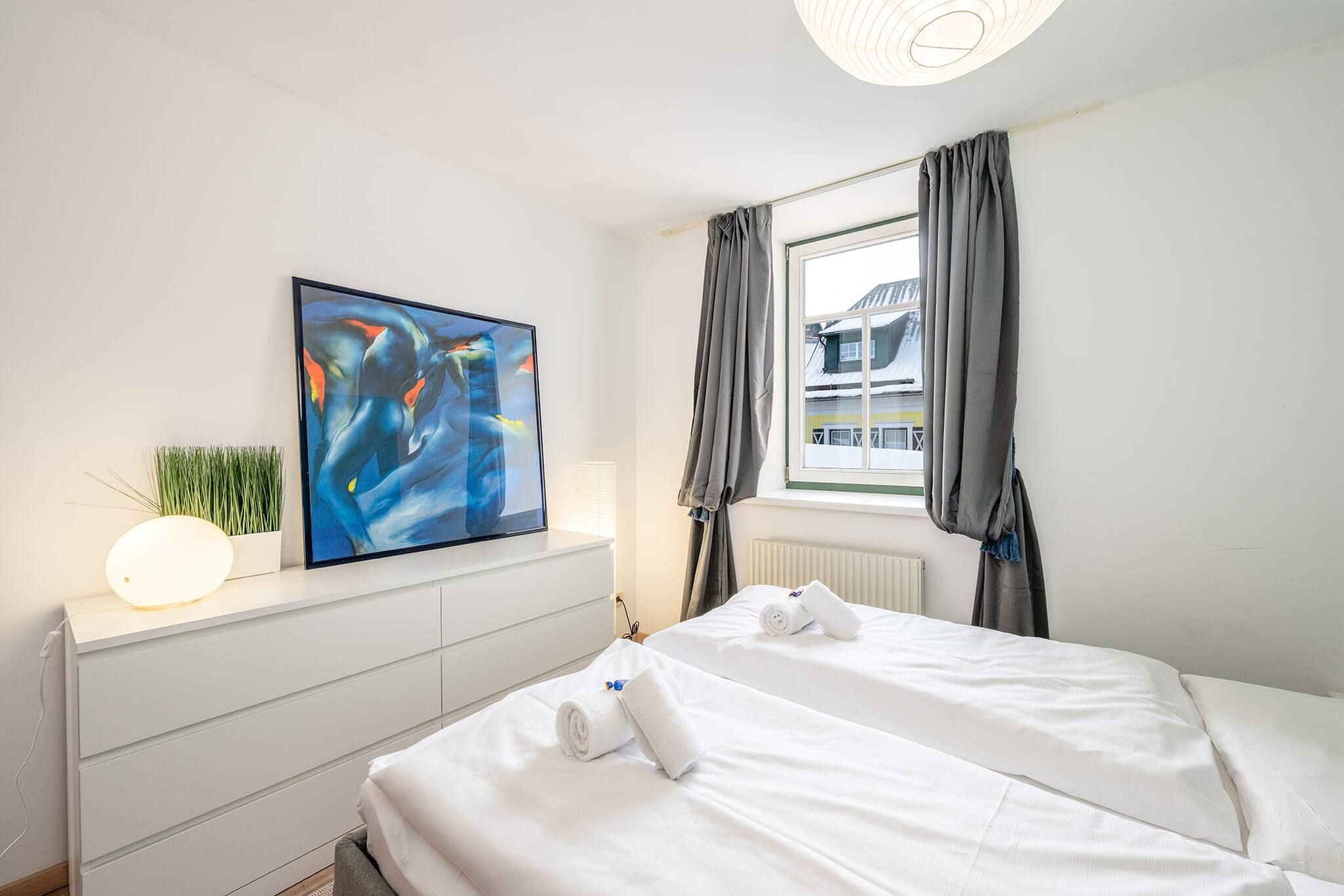 Una habitación de hotel con cama, un cuadro, una lámpara de noche y una ventana con cortinas.