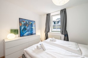 Una habitación de hotel con cama, un cuadro, una lámpara de noche y una ventana con cortinas.