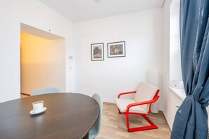 Una habitación con una mesa redonda, una silla roja, dos cuadros en la pared y un ventanal con cortinas.