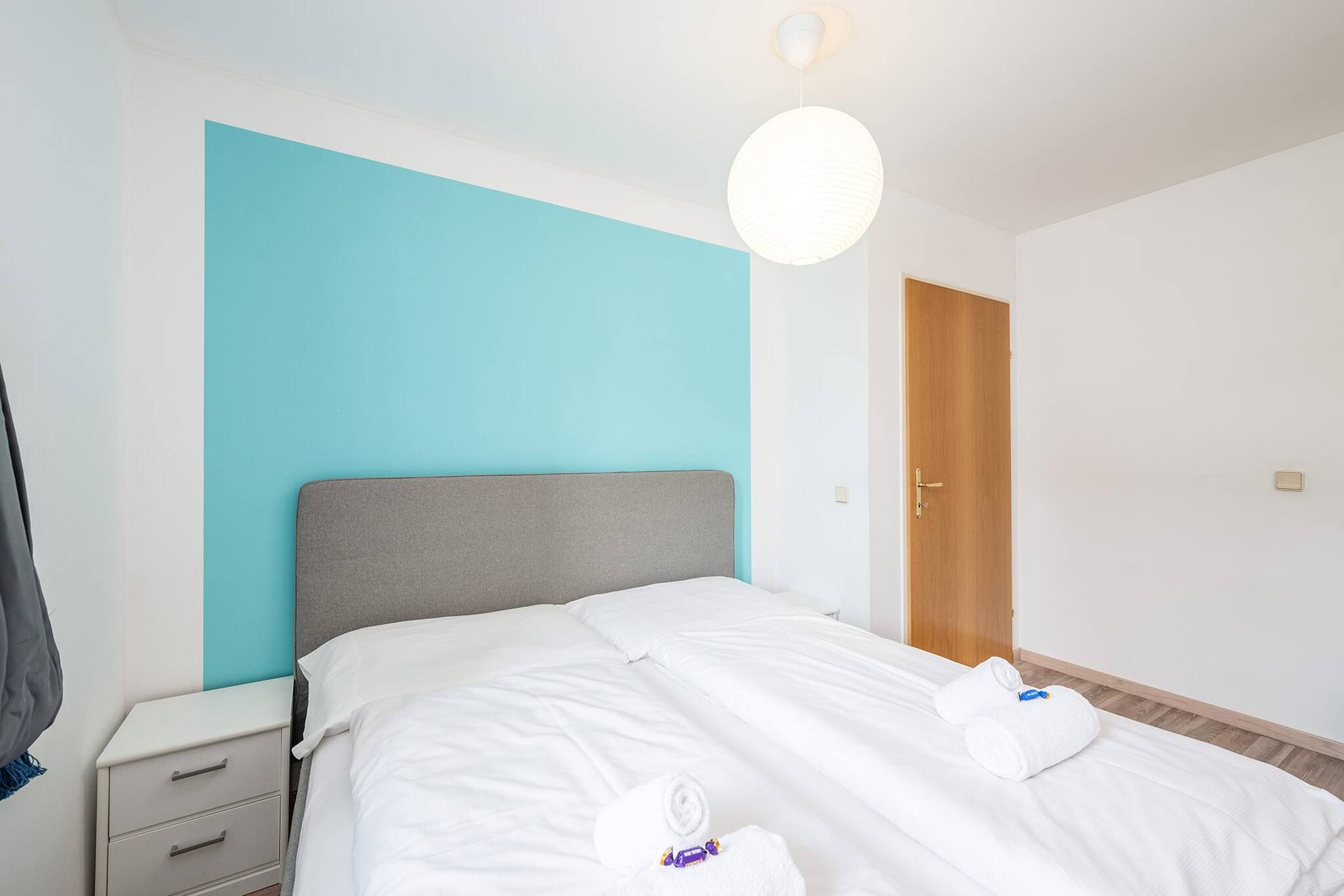Una habitación de hotel con una cama, una mesita de noche, una puerta de madera y una lámpara.