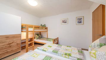 A dormitory room with bunk beds, a desk, and two framed pictures on the wall.