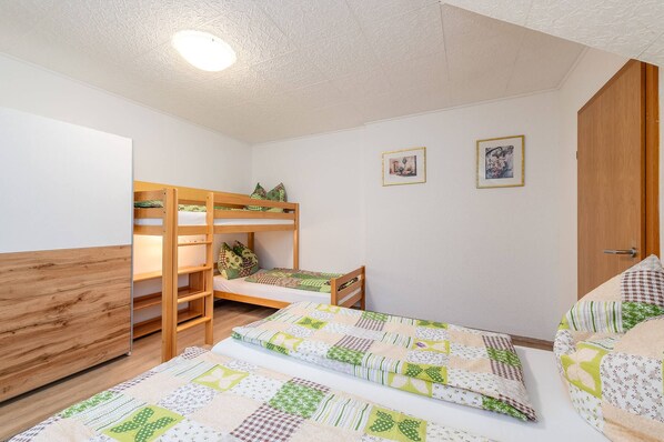 Ein Schlafsaalzimmer mit Etagenbetten, einem Schreibtisch und zwei gerahmten Bildern an der Wand.