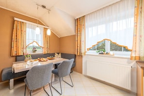 Ein Essbereich mit Tisch, Stühlen und Blick ins Freie durch große Fenster.