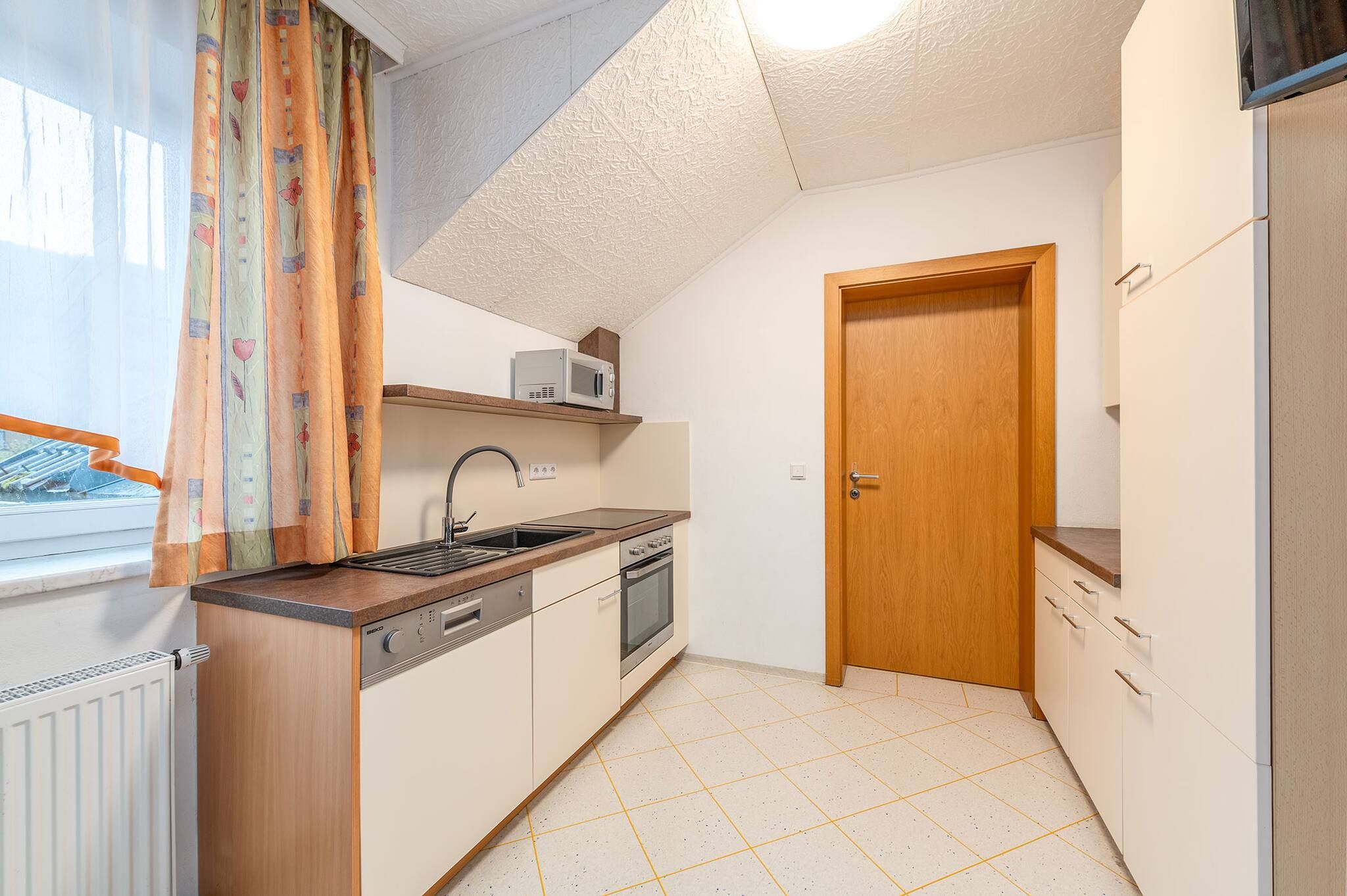 A compact kitchen with a microwave, oven, sink, and a wooden door.