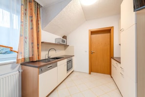 Eine kleine Küche mit Mikrowelle, Backofen, Spüle und einer Holztür.