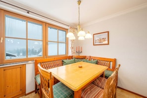 Ein Essbereich mit einem Holztisch und Bänken, einer Pendelleuchte und einem Fenster mit Blick auf eine verschneite Landschaft.