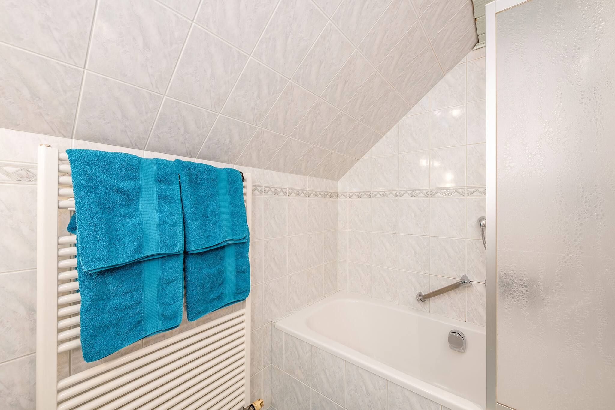 A bathroom with a bathtub, a shower, and a towel rack with blue towels.