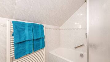 A bathroom with a bathtub, a shower, and a towel rack with blue towels.