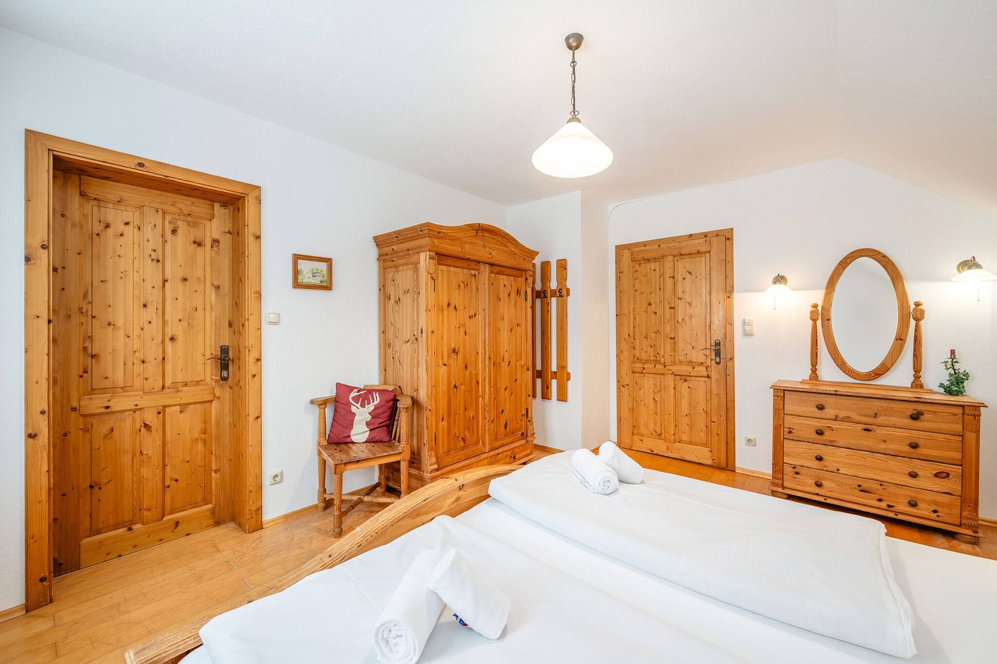 Ein Schlafzimmer mit Holztüren, einem Bett mit weißen Leinentextilien, einem Holzschrank und einem Spiegel.