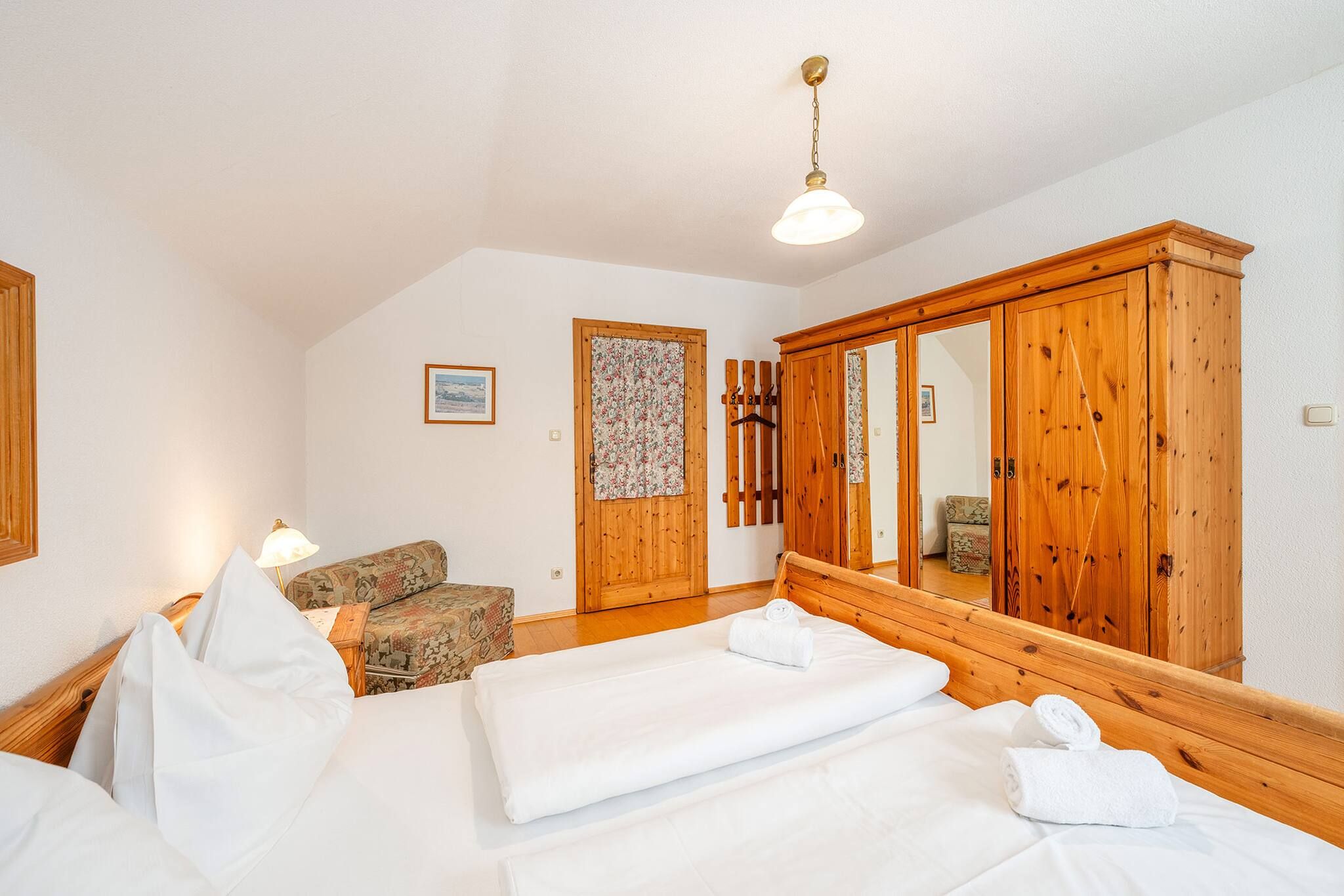 Une chambre d’hôtel avec un lit, une armoire en bois, une chaise et un porte-manteau mural.
