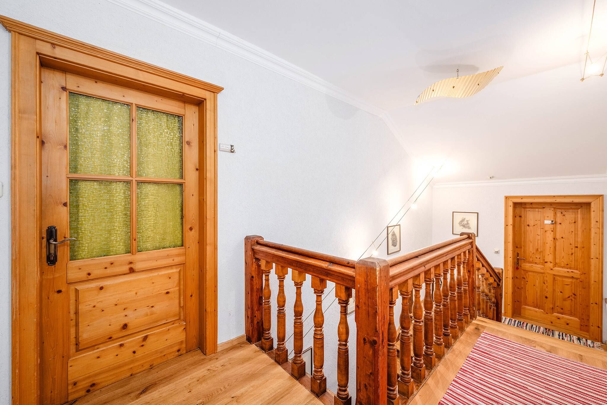 Eine Holztreppe mit Geländer, eine Glastür mit Holzrahmen und ein rot-weiß gestreifter Teppich auf dem Boden.