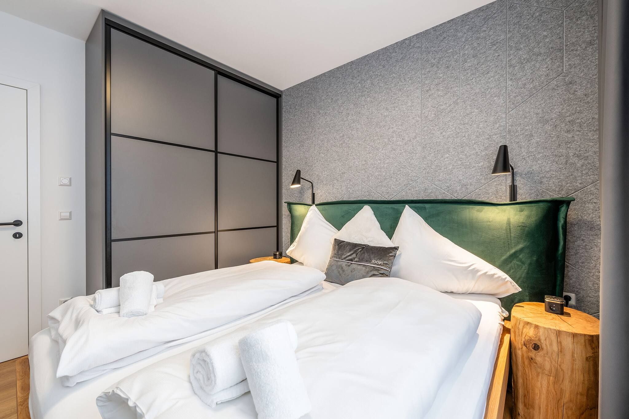 Ein modernes Hotelzimmer mit einer großen Schiebetür, einem Bett mit weißen Laken, zwei Nachttischlampen und einem grünen Kopfteil.
