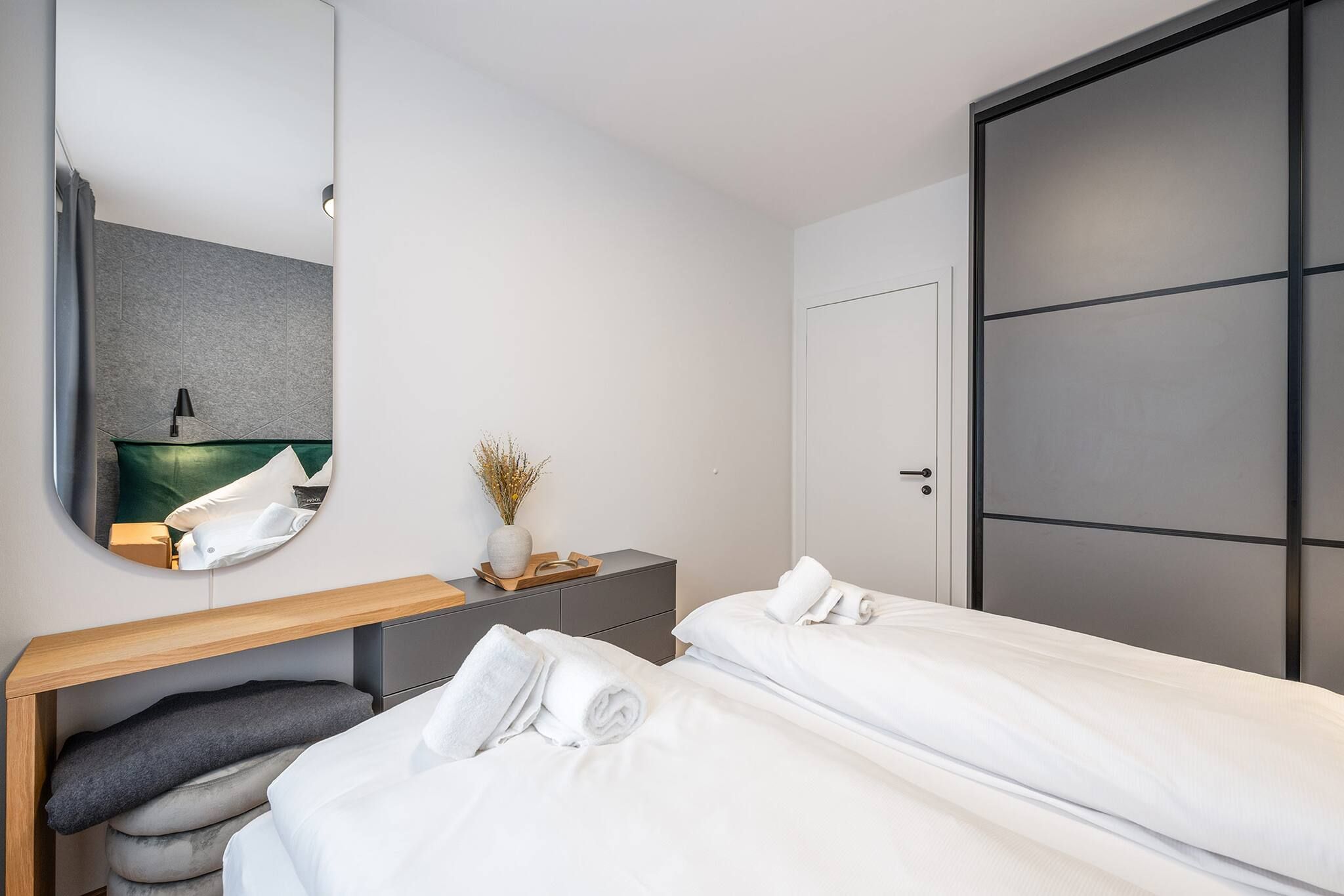 Une chambre d’hôtel moderne avec deux lits simples, une table de chevet avec une lampe, un miroir et une grande armoire.