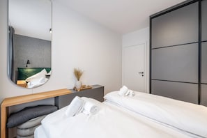 Ein modernes Hotelzimmer mit zwei Einzelbetten, einem Nachttisch mit Lampe, einem Spiegel und einem großen Kleiderschrank.