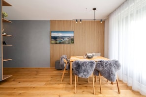 Ein moderner Essbereich mit einem Holztisch, Stühlen mit Felldecken, einem an der Wand montierten Fernseher und einer Wand aus Holzlamellen.