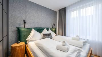 Een moderne hotelkamer met een groot bed, twee bedlampen, een houten nachtkastje en uitzicht op het landschap door dunne gordijnen.
