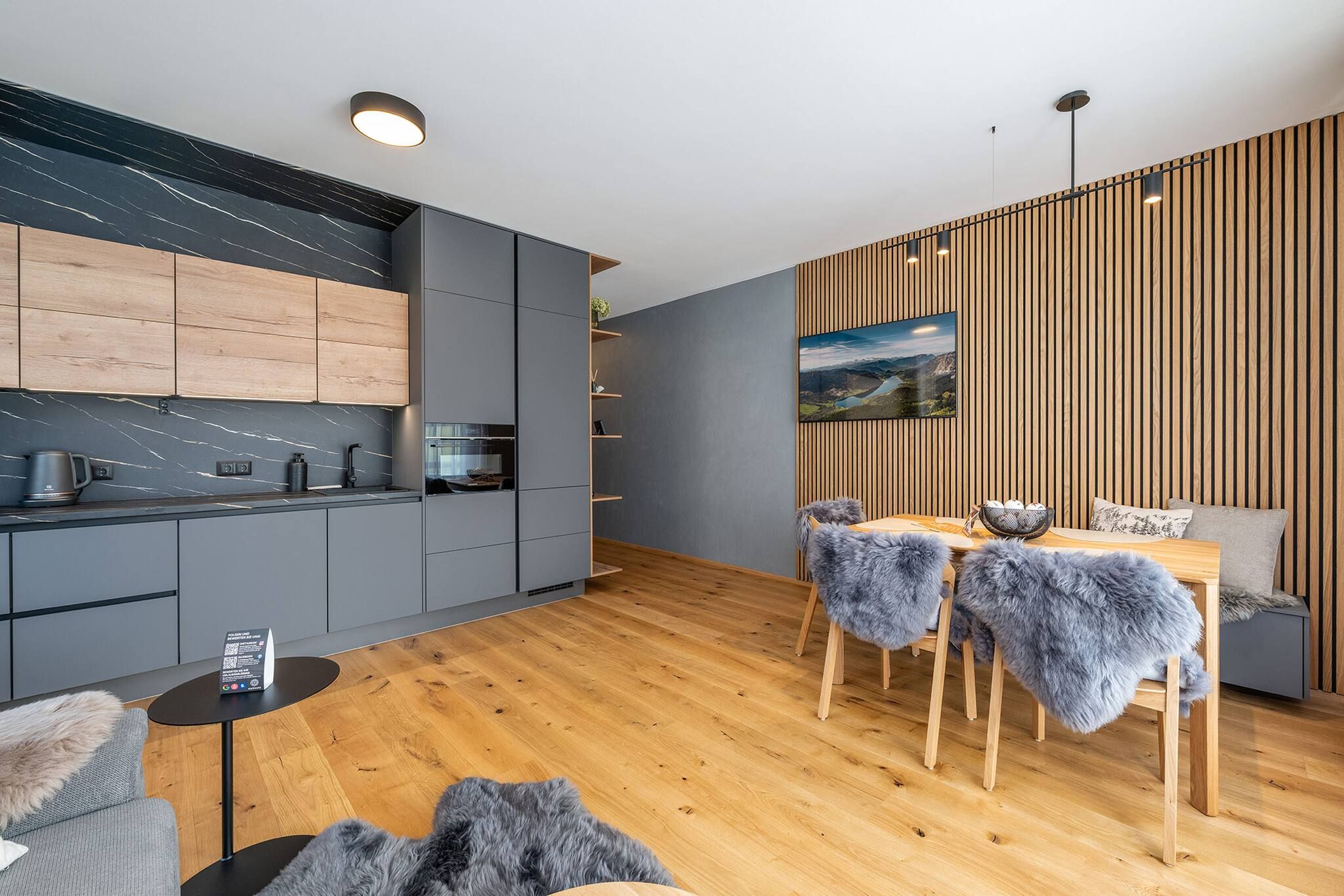 Een moderne keuken met grijze kastjes, een houten eettafel met stoelen en een houten vloer.