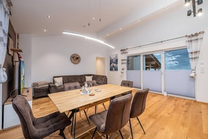 Een moderne woonkamer met een houten eettafel, bruine leren banken en een groot raam met uitzicht op bergen.