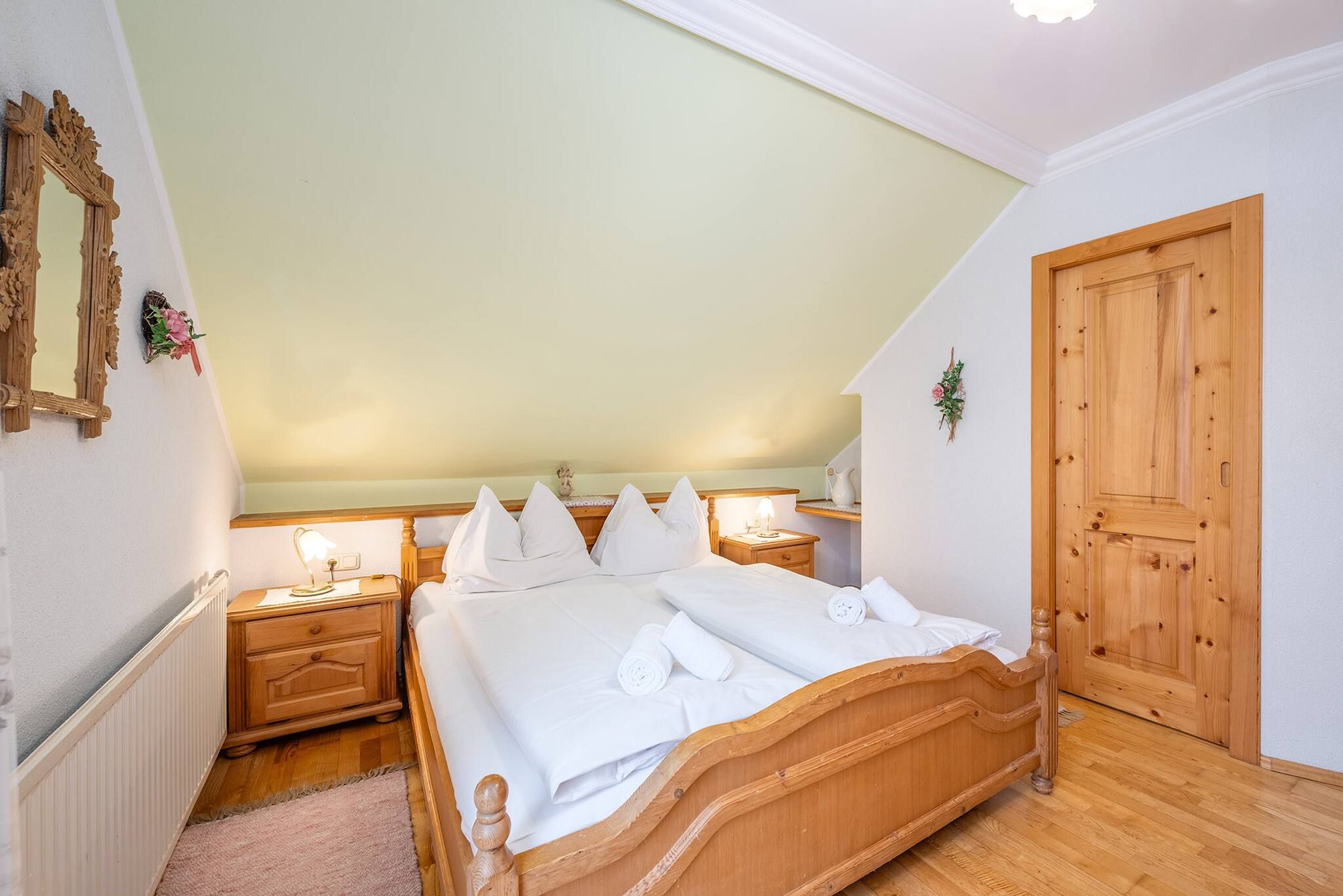 Ein Schlafzimmer mit einem hölzernen Bett, zwei Nachttischen, einem Heizkörper, einer Holztür und einem Spiegel an der Wand.