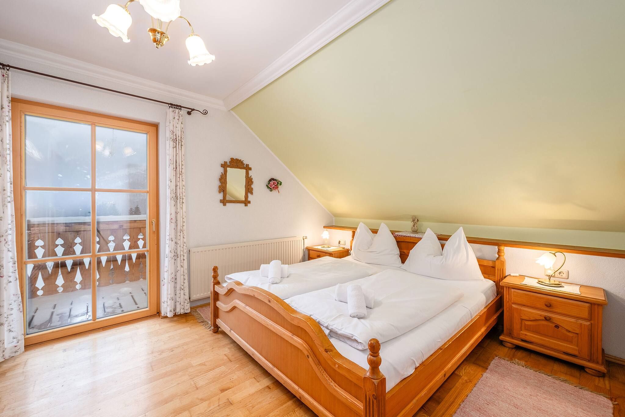 A bedroom with a wooden bed, a nightstand, a window with curtains, and a view of a balcony.