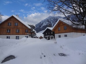 Ein verschneites Dorf mit Holzhäusern, ein Berg im Hintergrund und ein klarer Himmel.