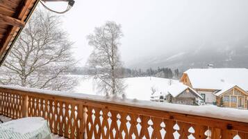 A wooden balcony with a lattice railing overlooking a snowy landscape with houses and trees.