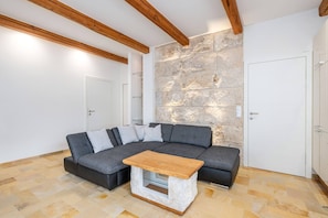 Una sala de estar moderna con un sofá seccional, una mesa de centro de madera y vigas de madera a la vista en el techo.