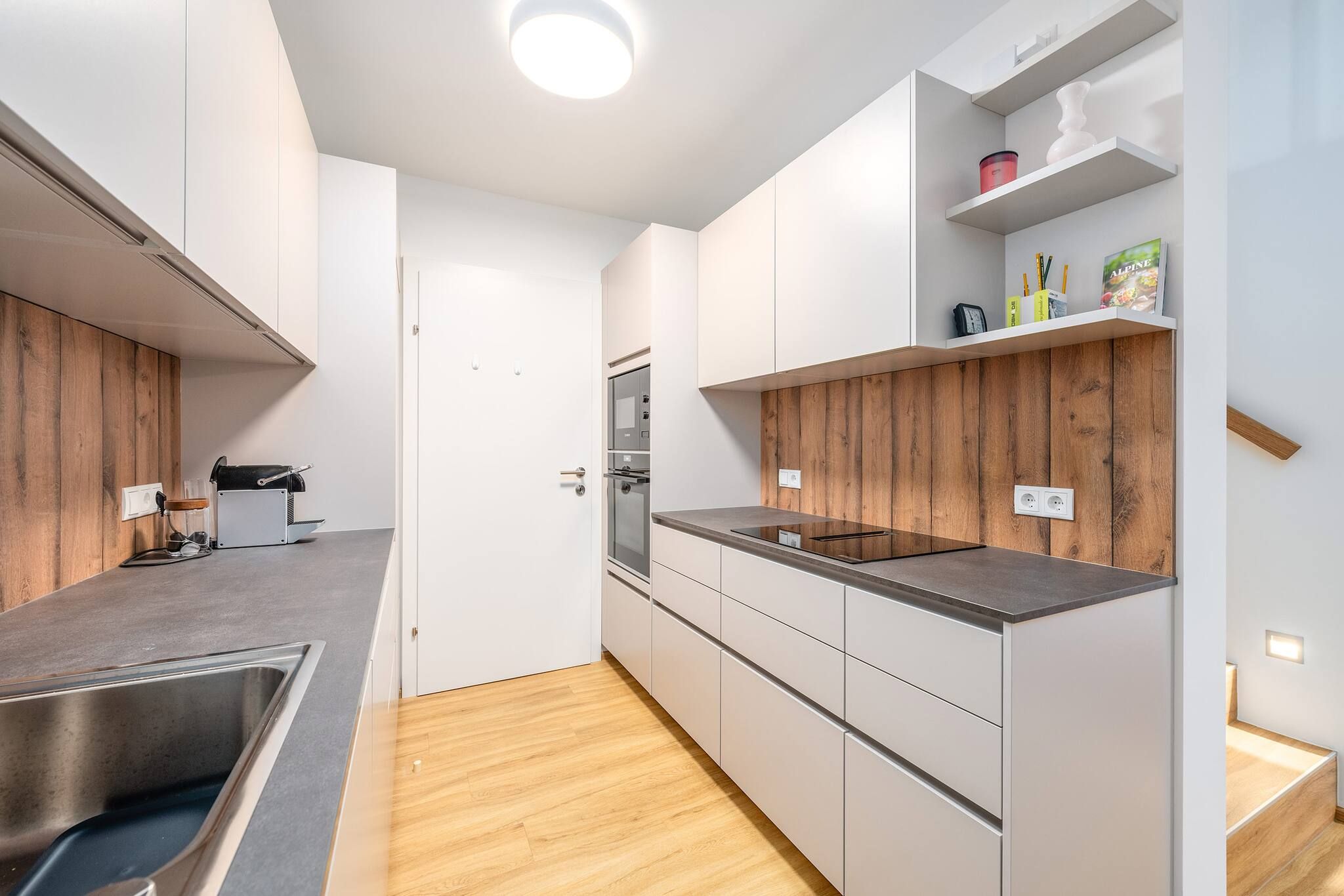 Eine moderne Küche mit weißen Schränken, einer Holzvertäfelung, einem eingebauten Ofen und einer Edelstahl-Spüle.