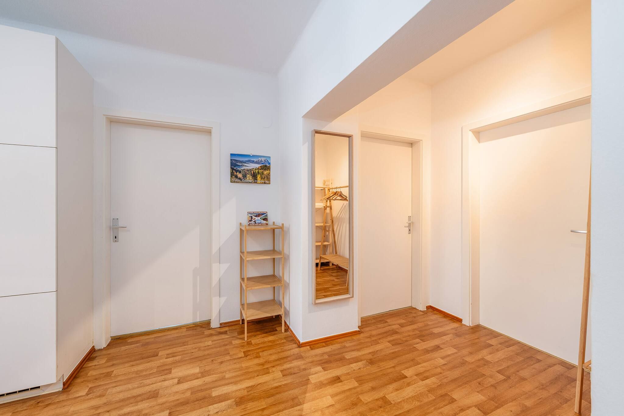 Un pasillo con piso de madera, paredes blancas y puertas que dan a otras habitaciones.