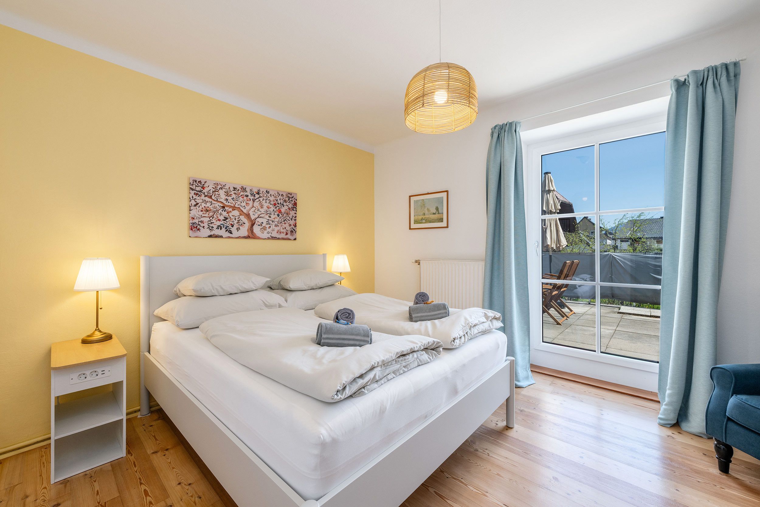 Una camera d'albergo con un letto, due lampade sui comodini, un quadro, una finestra con tende e vista all'esterno.
