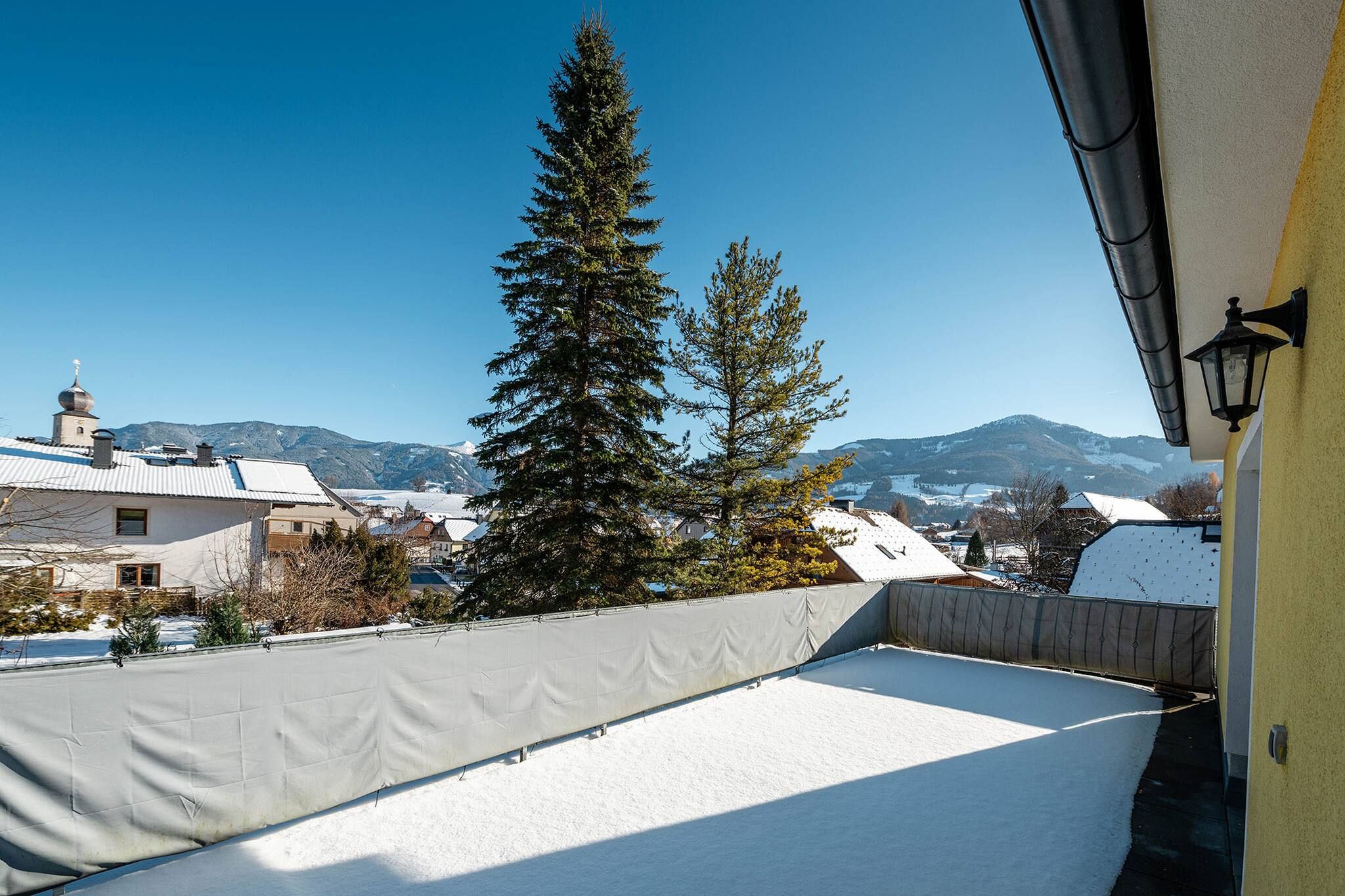 Ein mit Schnee bedecktes Dach mit Blick auf eine Stadt und Berge im Hintergrund.