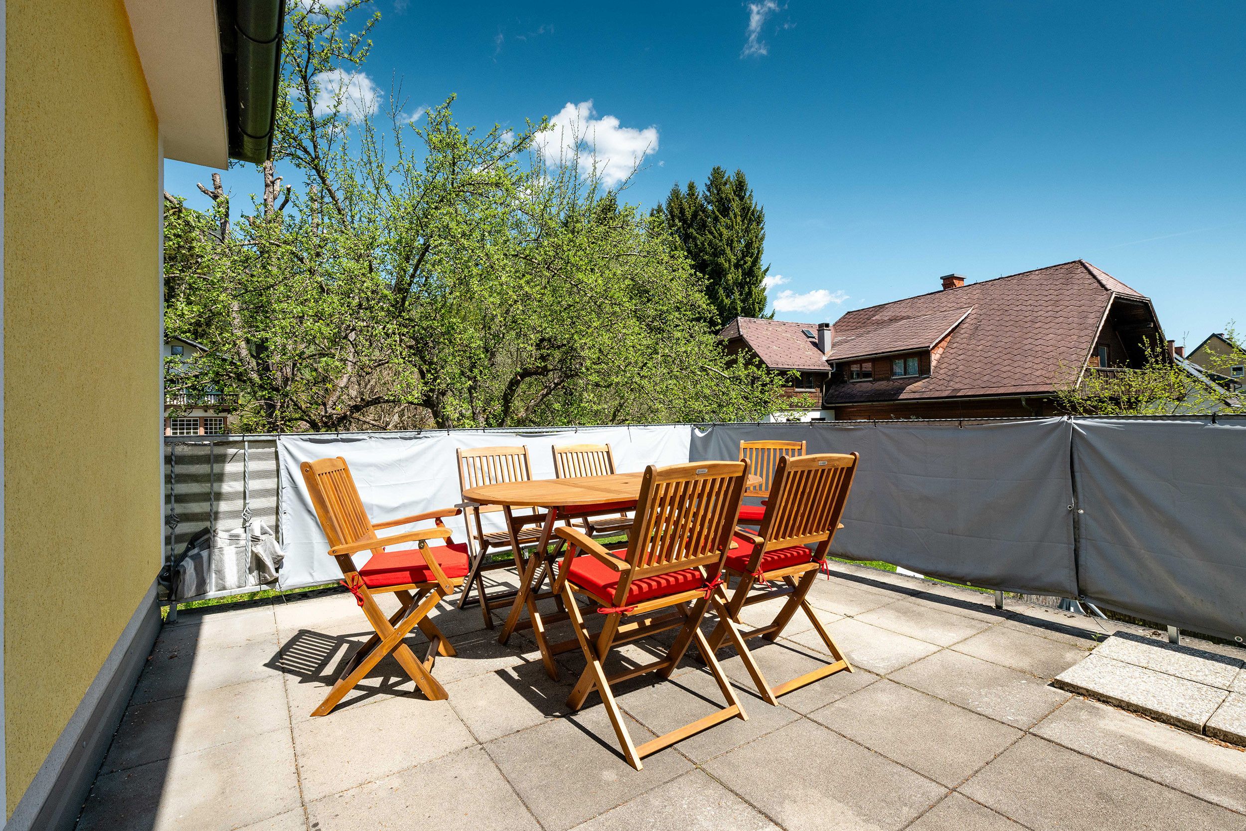 An outdoor patio with a table and chairs, a covered area, and a view of a house and trees.