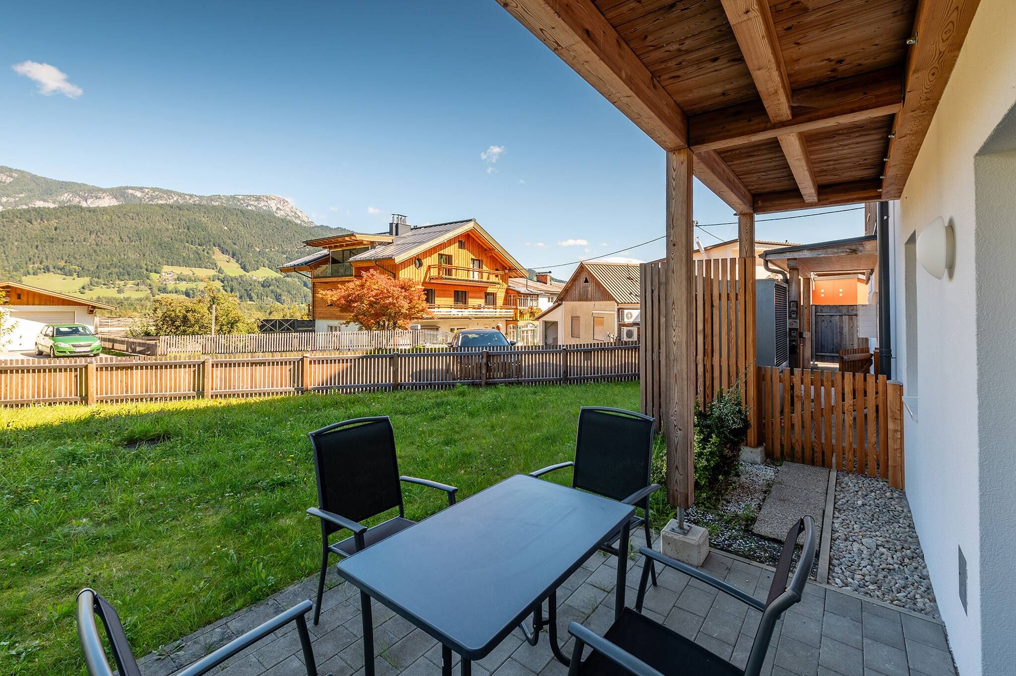Eine Terrasse mit Tisch und Stühlen, ein Holzzaun und Blick auf einen Berg und ein Haus.